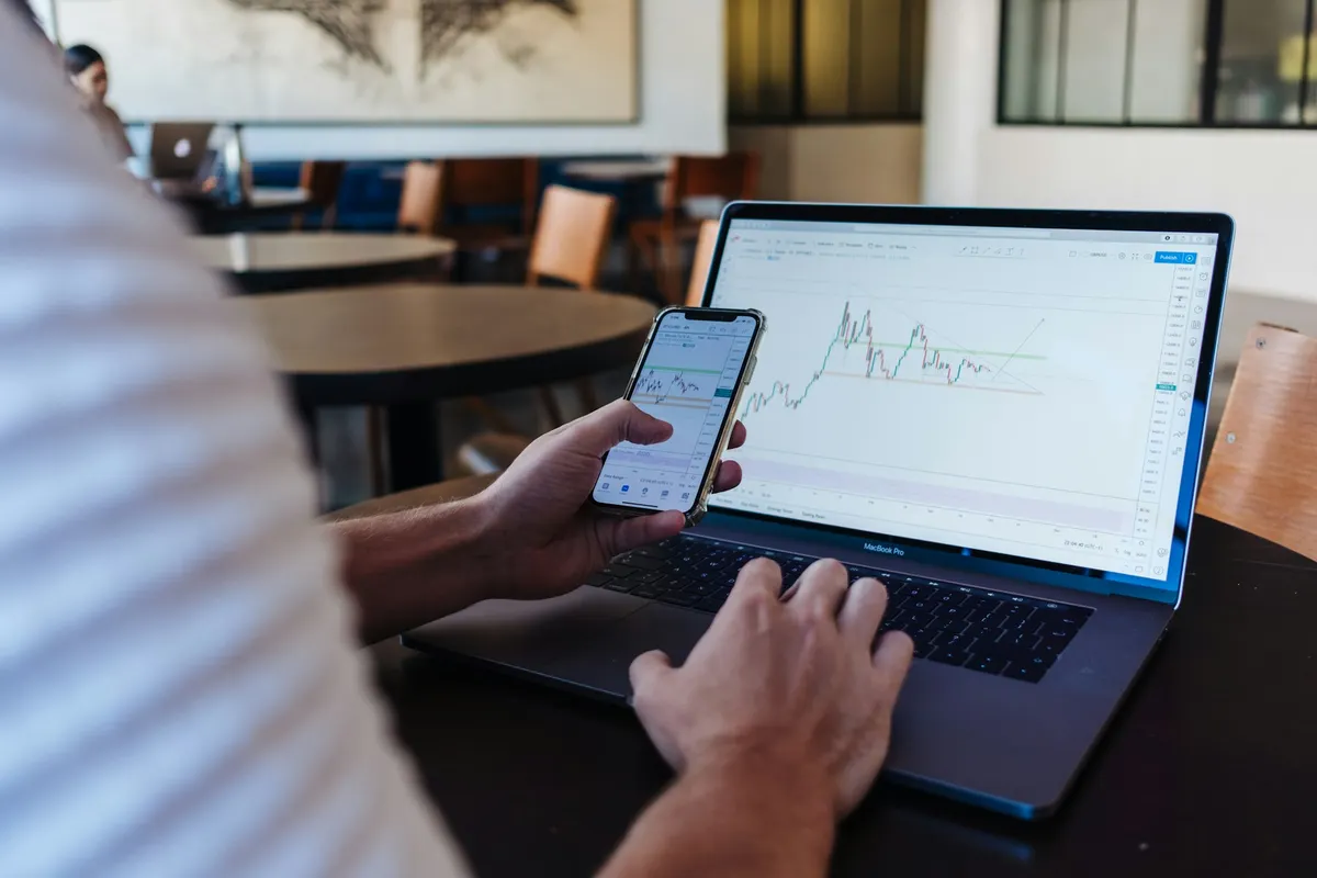 a man trading while holding a phone in front of a laptop